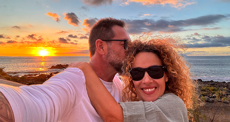 Glimlachend stel dat een selfie maakt tijdens hun vakantie, met de zee en de ondergaande zon op de achtergrond.