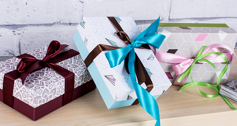 3 decorative boxes for photo prints in different themes with colourful ribbons on a wooden shelf; the brick wall in the background.