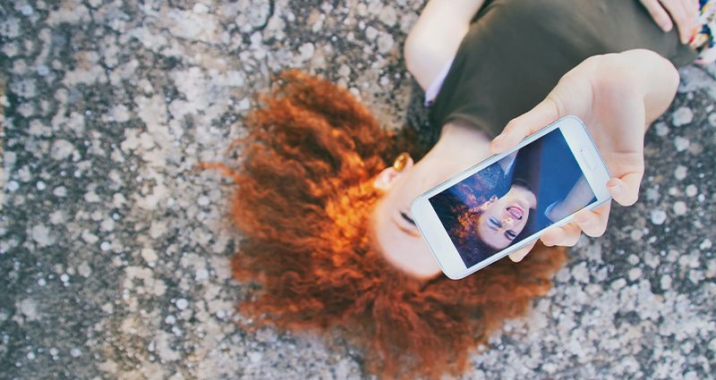 Close-up van een smartphone tijdens het maken van een selfie – een vage afbeelding van een jonge vrouw op de achtergrond.