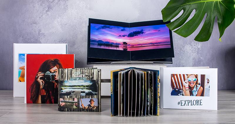 6 layflat albums in various formats on a desk; part of them are open, others are closed.