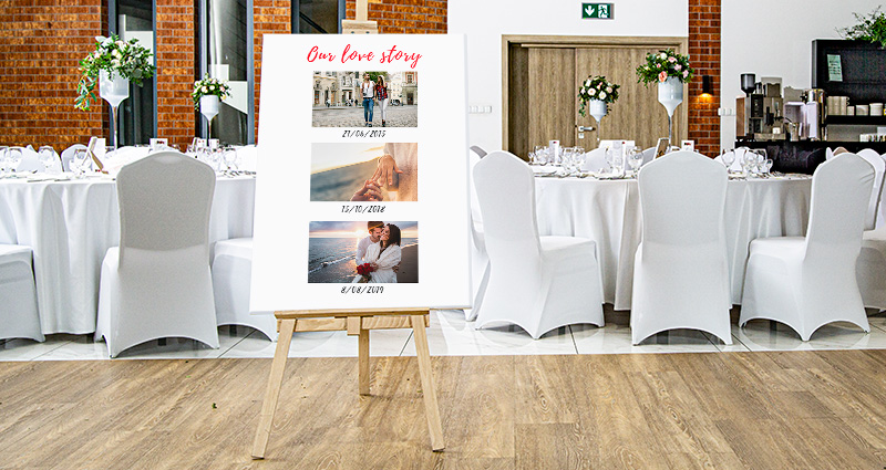 Une toile photo avec trois photos de jeunes mariés de différentes étapes de leurs vie, en haut le texte „Our love story”, en dessous des photos il y a des dates. Au fond des tables rondes décorées en blanc.