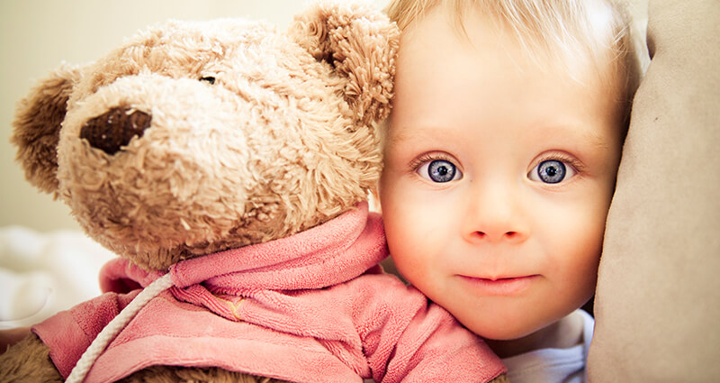 Ein Junge mit großen blauen Augen hält ein Teddybär