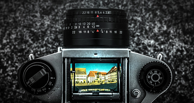 Una cámara fotográfica sobre el fondo de granito, en su pantalla se ve una foto de color de un edificio y de cielo azul – la foto tomada a vista de pájaro.