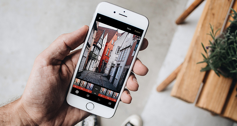 A close up on a smartphone held by a man in his hand. The smartphone displays colorful town houses. Aerial view.