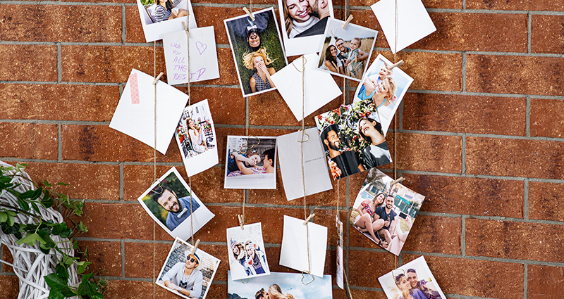 A close-up on Insta Photos presenting the wedding guests, all photos are attached to hemp strings. A brick wall in the background