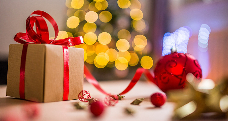 A gift with red ribbon with a Christmas tree in the background.