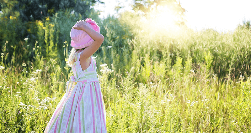 A girl dressed in a stripped dress, standing on a meadow.