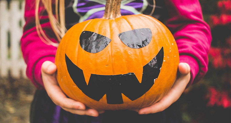 A girl holding a smiling pumpkin.