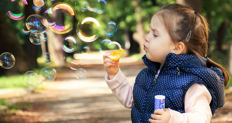 A girl making soap bubbles outside.