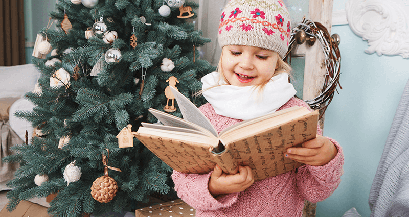 Ein Mädchen steht am Weihnachtsbaum und singt Weihnachtslieder