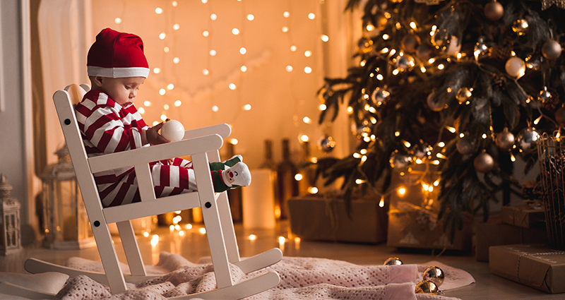 Malý chlapec v slavnostním pyžamu a klobouku Santa Clause, spí na houpacím křesle vedle vánočního stromku