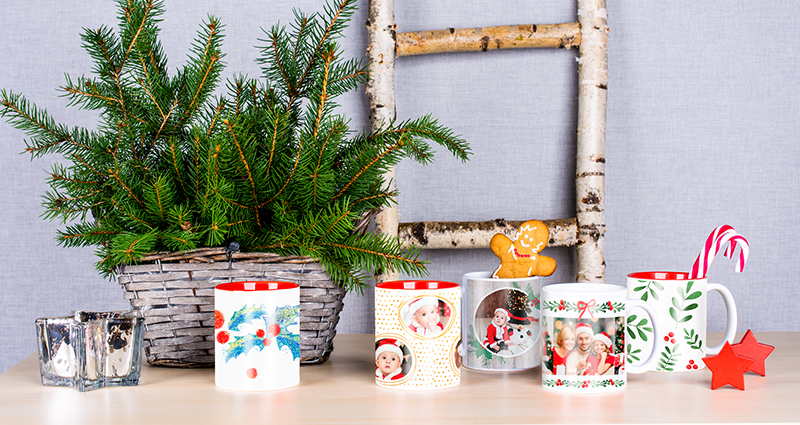 A photo showing Christmas photo mugs templates next to a candlestick and spruce twigs in a basket. There are sweets inside some of the mugs.