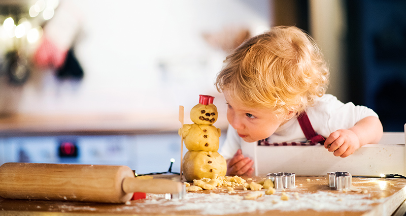 Een jongetje tijdens het bakken van kerstkoekjes. Ernaast een van deeg gemaakte sneeuwpop