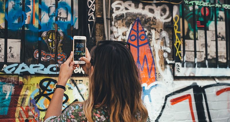 Una foto di una donna che fotografa un murales sul muro di un palazzo