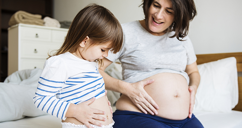Nėščia moteris rodo mažai mergaitei savo pilvą