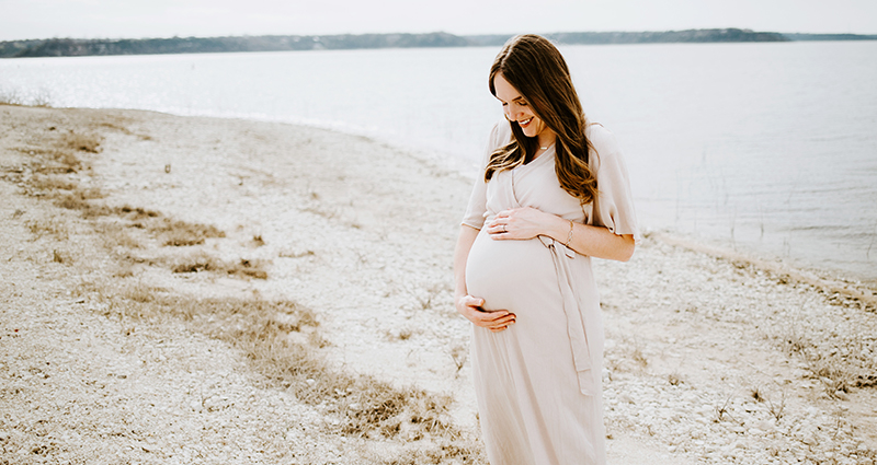 A pregnant women in a summer dress on the beach