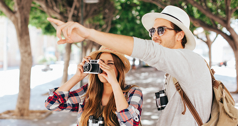 Turistų pora atostogose, vyras rodo kažką toli, o mergina fotografuoja