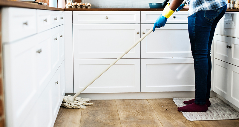 Een vrouw die de vloer in de keuken schoonmaakt; rond de witte keuken kastjes.