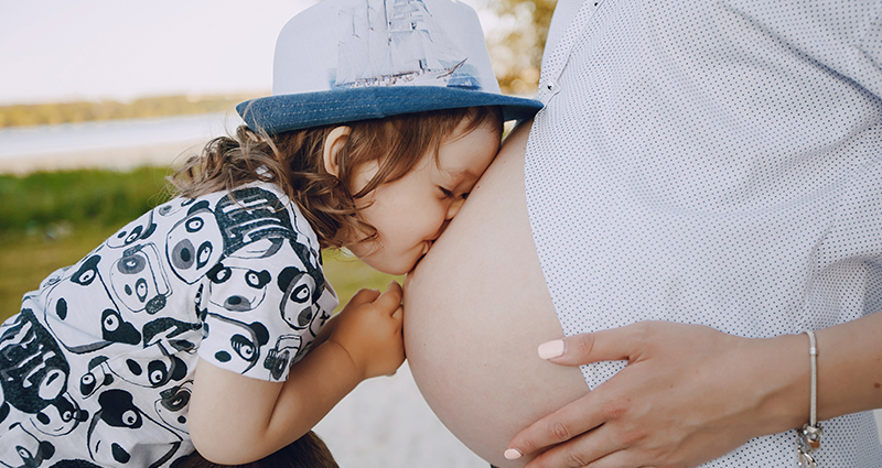 Mažas berniukas bučiuoja nėščios motinos pilvą