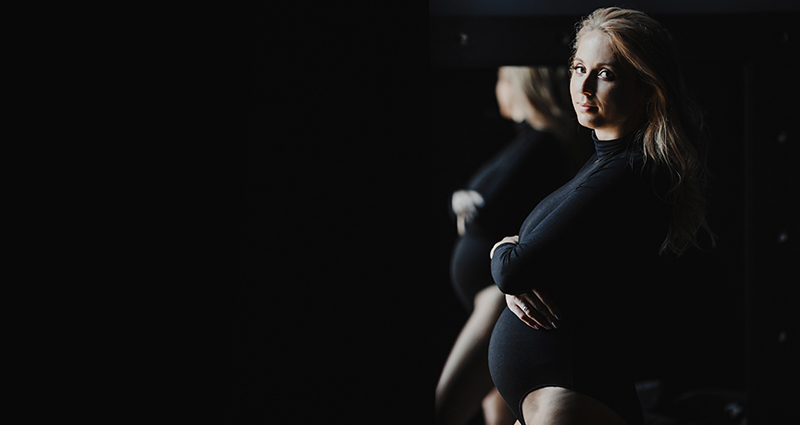 Eine junge schwangere Frau in einem schwarzen Body während eines Fotoshootings in einem Studio