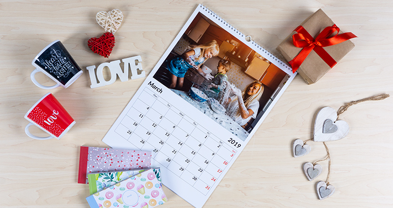 Un calendrier photo A4 sur un mur blanc, des livres photo, des albums et d’autres sur une étagère