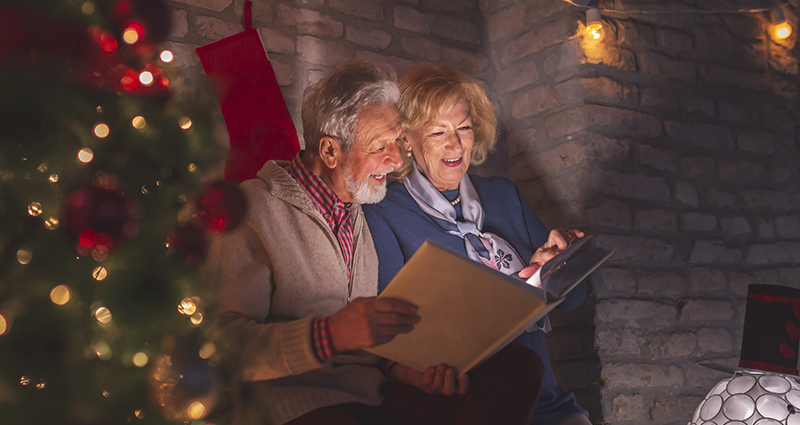 Un couple de personnes âgées regarde un album photo rempli des expressions amusantes de Noël