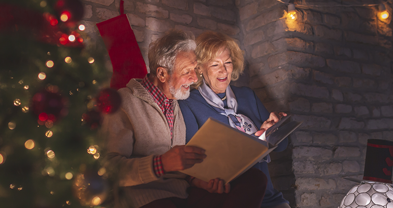 An elderly couple looking at a photo album filled with funny Christmas captions