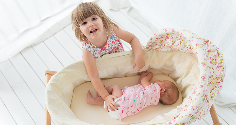 An infant in a cradle, a little girl standing next to it