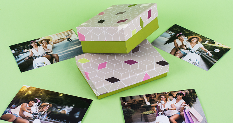 Boxes for photo prints with mosaic theme in two sizes, next to them spread photo prints – green background.Bilderbox Mosaik in zwei Größen und ein paar Fotoabzüge im grünen Hintergrund