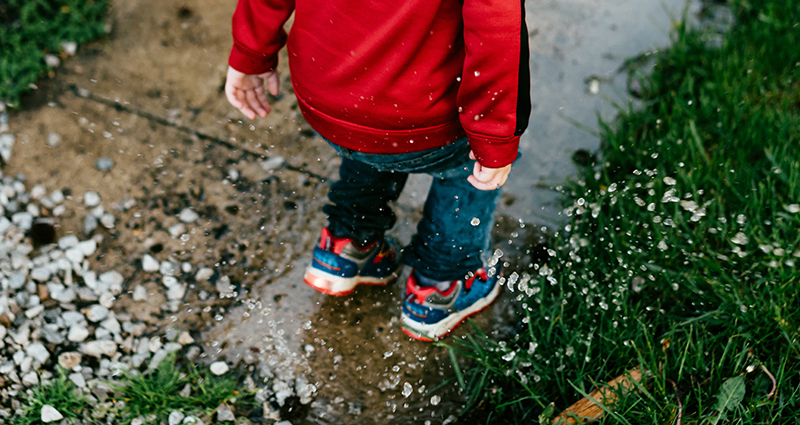 Kleiner Junge springt in eine Pfütze