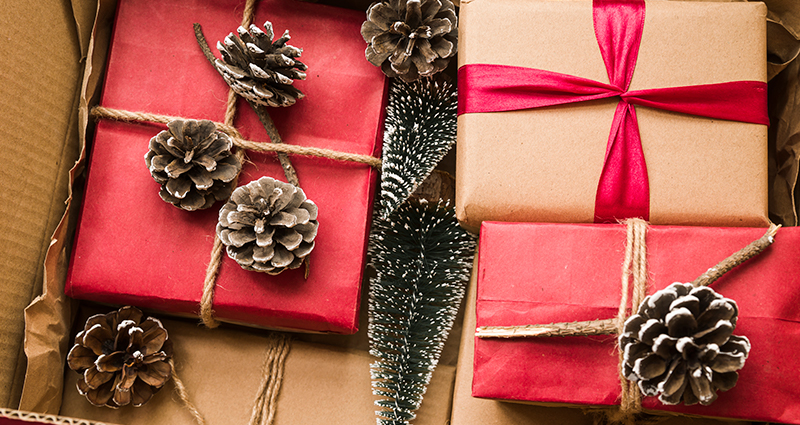 Regalos navideños envueltos en papel gris y rojo, atados con la cuerda. Unos conos al lado de los regalos.