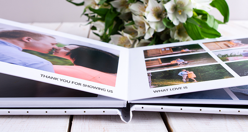 Close up on an open Luxury Album with photos of a couple. White flowers bouquet in the background.