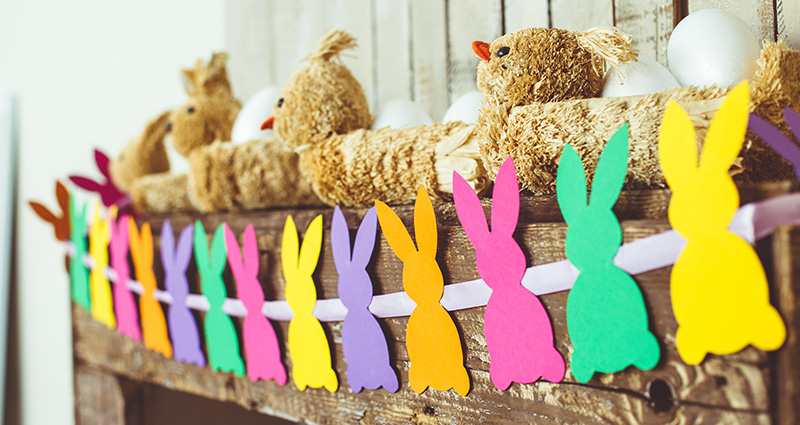 Eine Girlande mit bunten Papierhasen, die auf einem Holzbalken mit Osterdekorationen aufgehängt wurde.