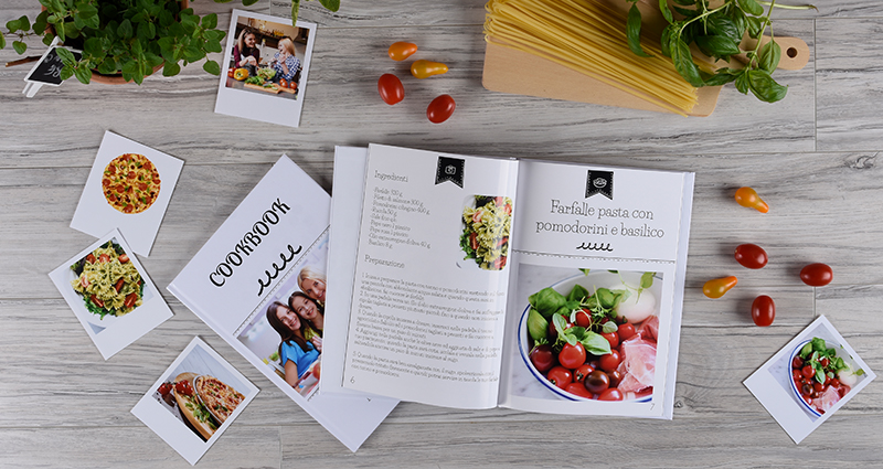 Cookbook lying next to retro prints of food, herbs, pasta and cherry tomatoes.