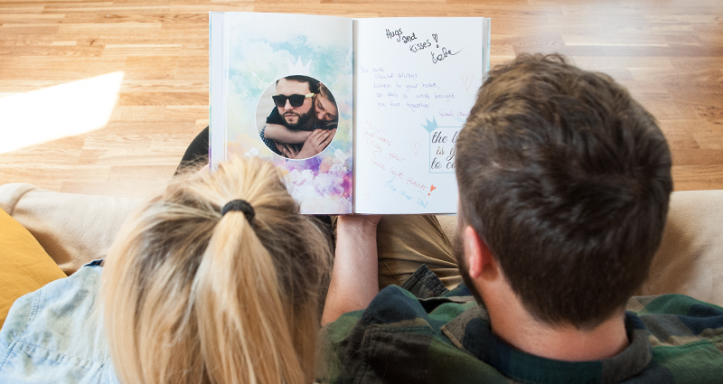 Un couple assis sur le canapé regardant leur livre d’or  - photo prise de derrière.