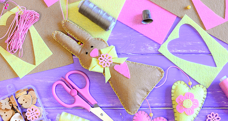 Easter bunny made of felt. Threads, scissors, wooden buttons and colourful sheets of felt laying around.