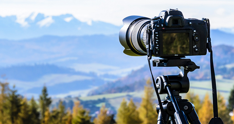 Primo piano della fotocamera su un treppiede, sullo sfondo la foresta e le montagne