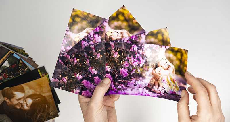 Enfoque a las manos tomando 4 fotos iguales impresas en varios tipos de papeles. A la izquierda hay otras fotos puestas en forma de abanico.