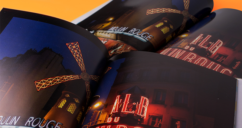 Detailní pohled na dvě knihy se stejnou fotkou větrného mlýna Moulin Rouge. Jedna kniha vytištěná v 7C, druhá tradičním způsobem na stroji XEROX.
