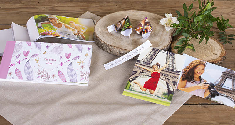 Galletitas chinas hechas de fotos en un disco de madera; alrededor de ellas, unas fotos y Sharebooks. Junto con la ramita verde. Composición sobre un mantel beige en una mesa de madera.