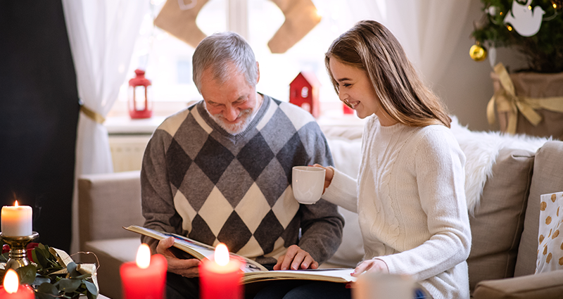 Grandfather and granddaughter looking at photo album filled with funny Christmas captions