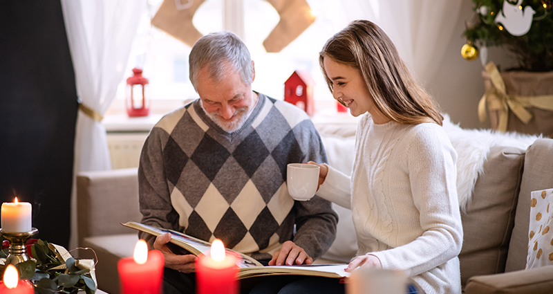 Abuelo con su nieta viendo un fotoalbum lleno de divertidas inscripciones navideñas