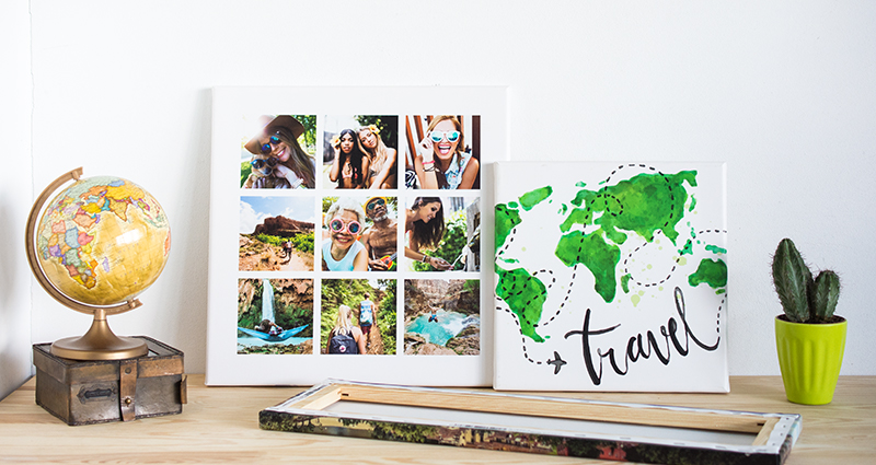 Holiday photo canvases on the desk, the landscape one lying, turned upside down, two other leaned against the wall (one of them shows a world map, the second one with a photo collage); a globe on a retro box on the left, a cactus in a green flowerpot on the right.