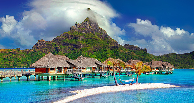 Wasserbungalows, azurlbaues Ozeanwasser und grün bewachsenes Gebirge im Hintergrund