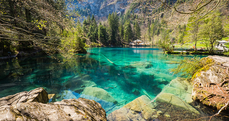 Modrý povrch jezera Blausee, v pozadí hory.