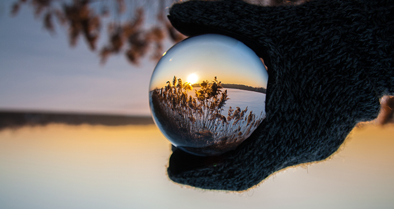 Un lac et des fleurs réflétés dans une bulle de verre tenue par une main dans un gant.