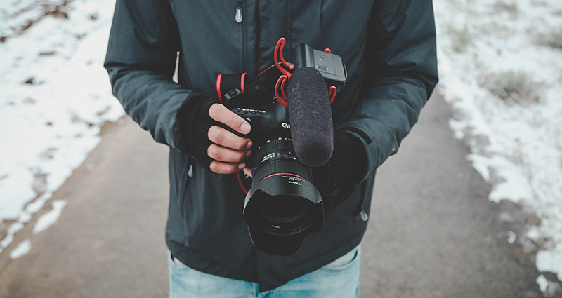 Un homme tenant un appareil photo dans les mains en gants sans doigts