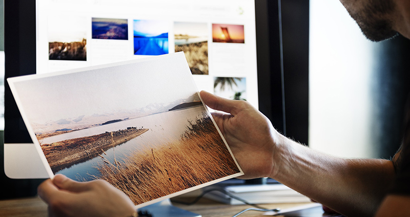 Hombre mirando una foto de gran formato, una pantalla con otras fotos en el fondo.