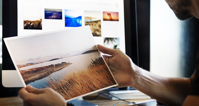 Muž se dívá na velkoformátovou fotografii, v pozadí monitor s ostatními fotografiemi.