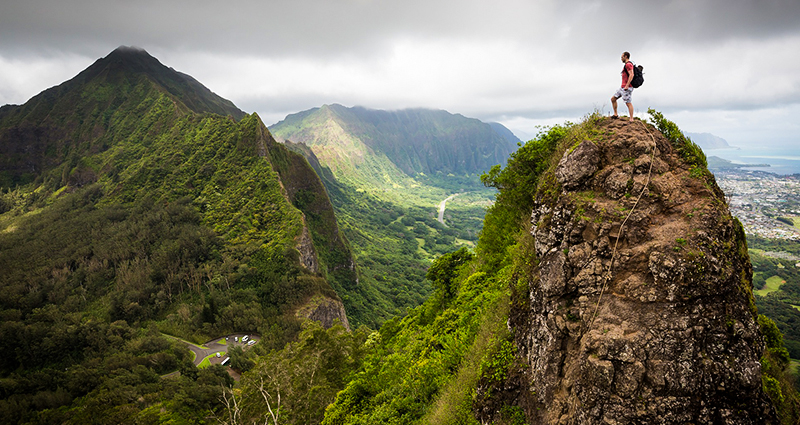 Man with a backpack standing on the top of the mountain, dark clouds in the background